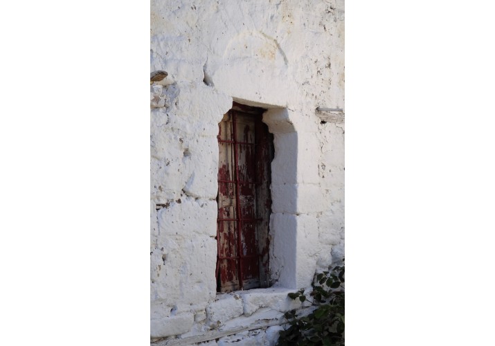 Παράθυρο με το χαρακτηριστικό σχήμα των λίθων και το τόξο. Διακρίνονται και το καρφωτό πατζούρι και τα κάγκελα.